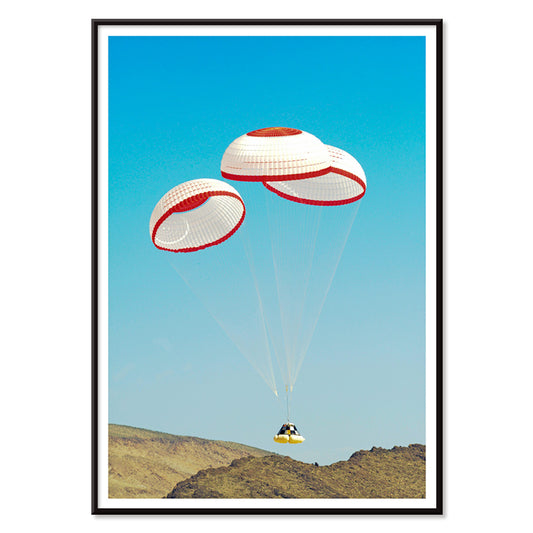 CST-100 crew capsule landing with three parachutes over desert landscape by NASA and The Boeing Company poster artwork, with black aluminium frame on white background