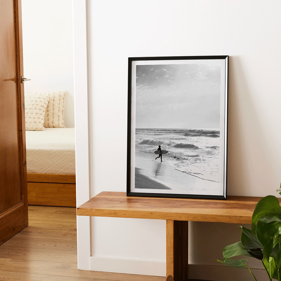 Black and white poster of a surfer with a board entering the ocean titled Surfer in Portugal by artist Black, framed and displayed in home decor