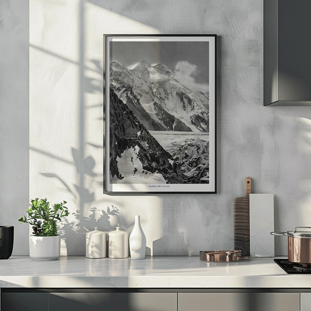 Black and white photograph and poster of Broad Peak by Vittorio Sella showing snow covered mountains and mountaineers climbing amidst rocky terrain and glacier, framed and displayed in home decor