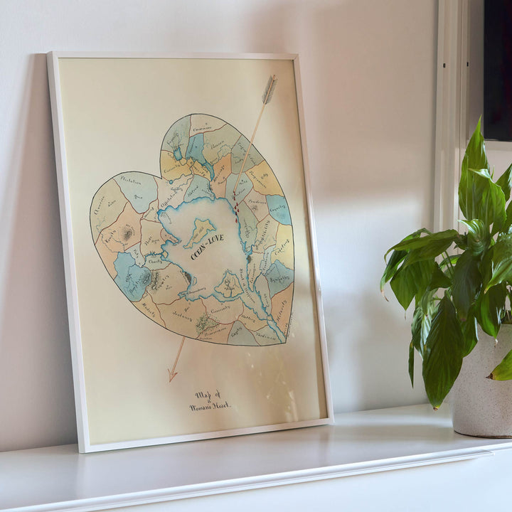 Joseph Husson Map of a Womans Heart 2 poster featuring a heart shaped map with an arrow, soft pastel blue and beige details, vintage style, framed and displayed in modern living room decor