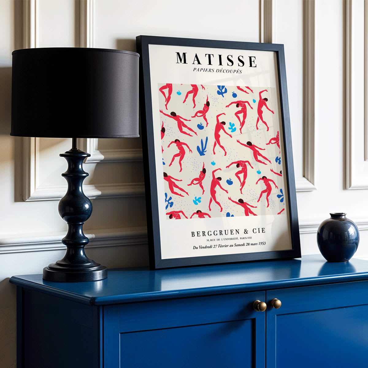Henri Matisse Dancing Figures Exhibition Poster with vibrant red and blue design featuring red cut out figures on a patterned background with exhibition details, framed and displayed in modern living room decor