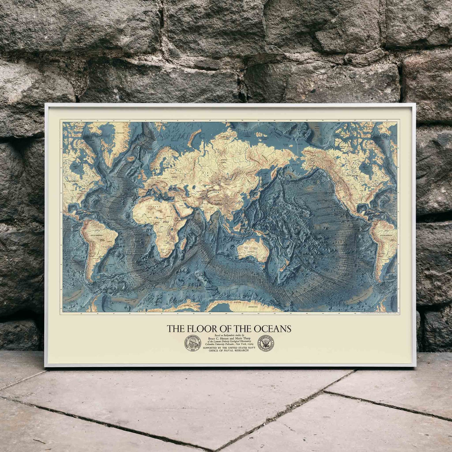 World map artwork showing ocean floors titled The Floor of the Oceans bathymetric map poster, framed and displayed in home decor