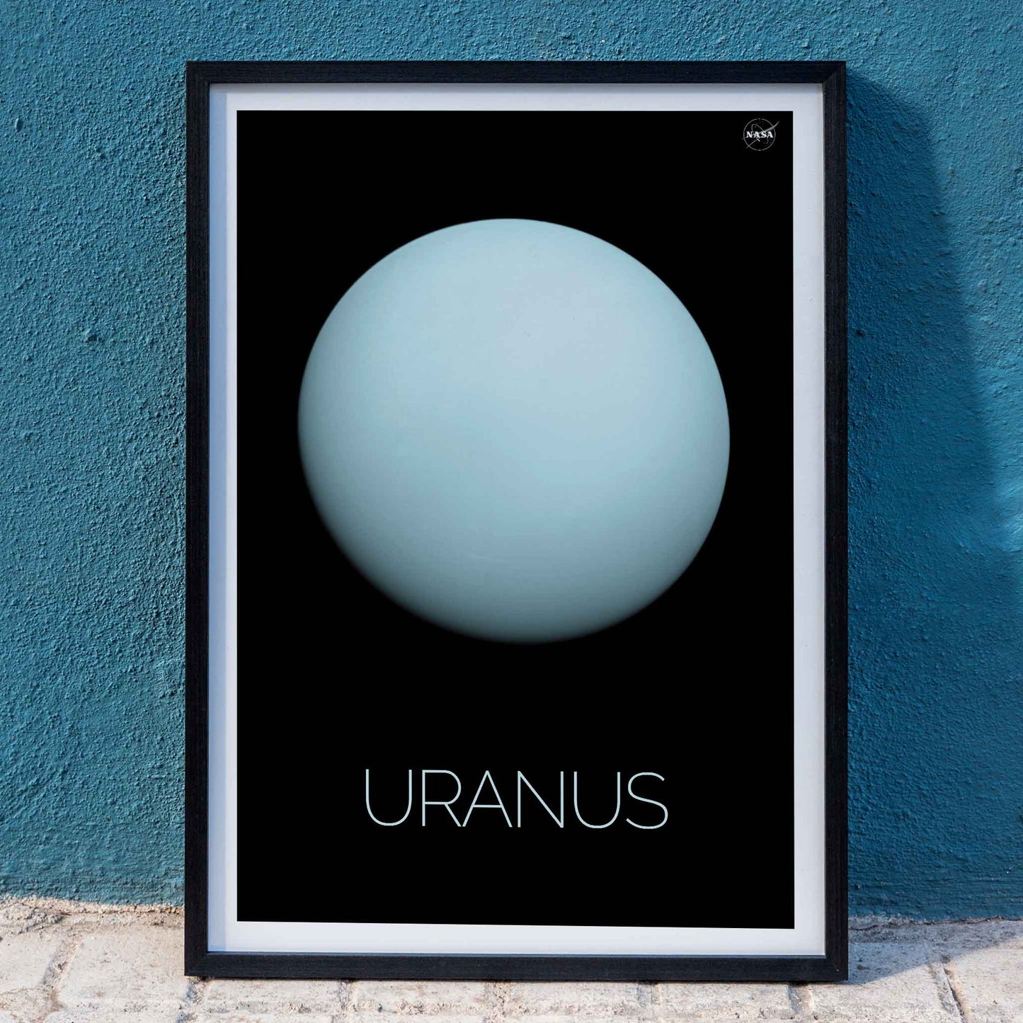 NASA poster of the planet Uranus featuring a light blue sphere against a black background with the title Uranus, framed and displayed in home decor