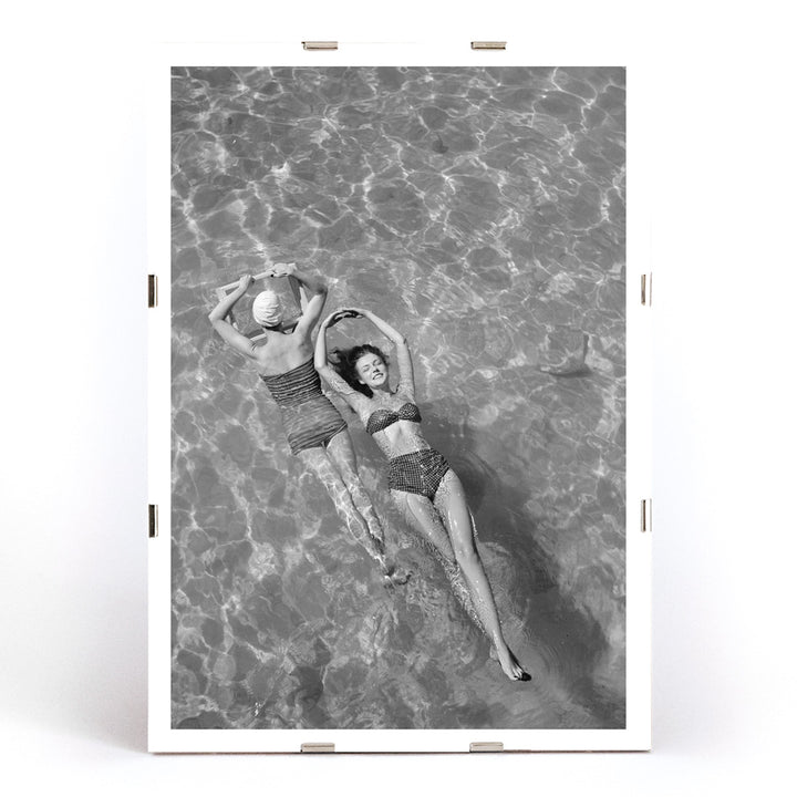 Fashion models in vintage bathing suits floating in a swimming pool artwork by Toni Frissell, framed and displayed in modern living room decor